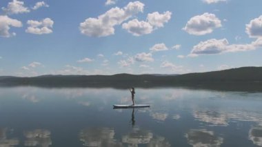 Beyaz bir kadının gölde yüzen sörf tahtası üzerinde sörf yaptığını gösteren sahneler dizisi.