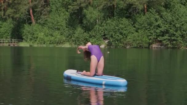 若い健康な女性が湖でボード上のアップボード上でアサナをストレッチと練習を行うことを示すショットのシーケンス — ストック動画
