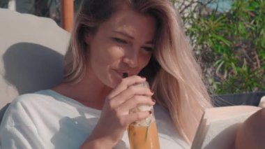 Orta ölçekli bir yakın plan, genç manken kokteyllerini yudumluyor ve lüks bir tatil köyünde gülümsüyor.