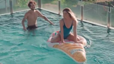 Yüzme havuzunda dondurmalı su yatağı süren ve onu iten genç ve havalı bir çiftin yüksek açılı görüntüsü.