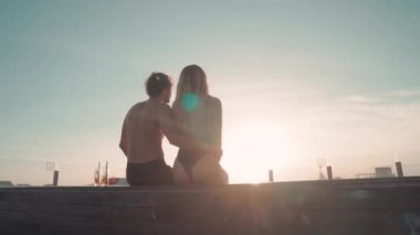 Yaz çifti, lüks bir tatil köyünde havuzun kenarında oturup güneşin batışını izlerken arka plan görüntüsü.