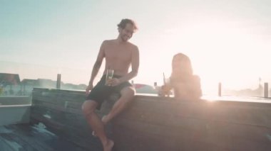 Lüks bir tatil köyünde havuz başında oturup gülen mutlu çiftin bebeklik fotoğrafı.