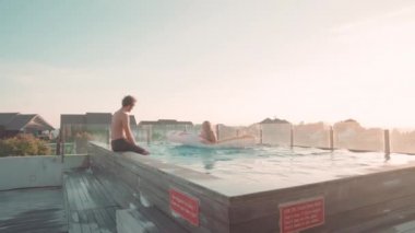 Yazın yüksek açılı çekimleri mutlu çiftin yüzme havuzunda serinlerken suya atlarken ve gülerken.
