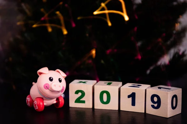 pink toy pig next to cubes on which is written in 2019 on the background of Christmas lights
