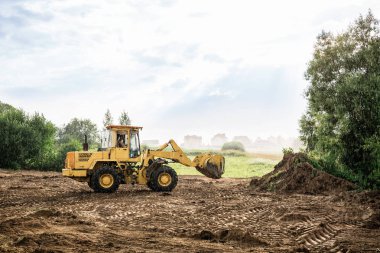 large yellow wheel loader aligns a piece of land for a new building clipart