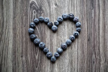 Olgun lezzetli böğürtlen ve çilek kalp şeklinde ahşap bir masa üzerinde