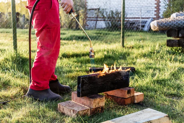 Человек сжигает деревянные доски пропаном по старинной японской технологии, создавая облицовочный материал для строительства дома — стоковое фото