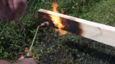 Bir adam eski Japon teknolojisini kullanarak propan ile ahşap plakalar yakar, bir ev inşa etmek için karşı karşıya malzeme oluşturma