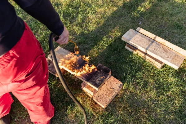 Человек сжигает деревянные доски пропаном по старинной японской технологии, создавая облицовочный материал для строительства — стоковое фото