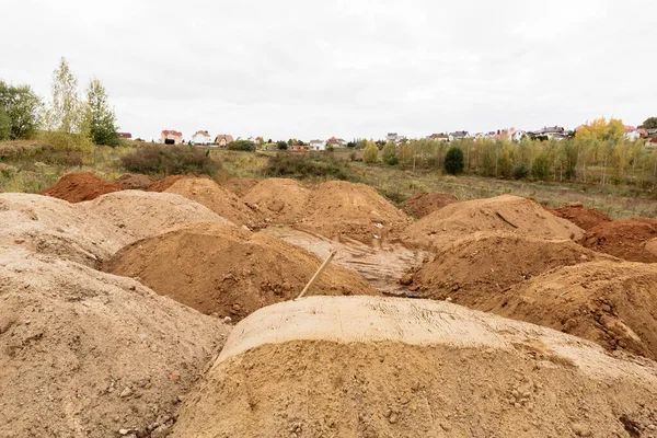 On a plot of land allotted for the construction of house lies a lot of piles of sand.