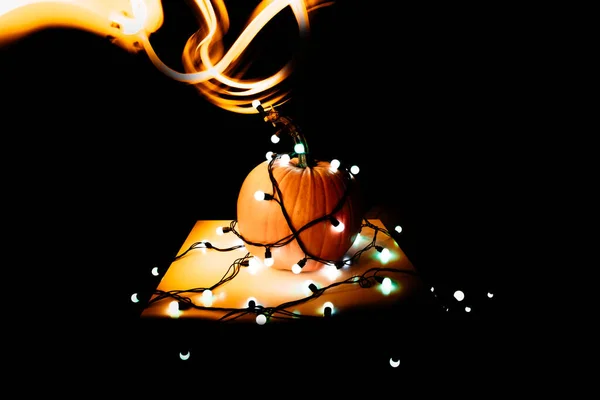 Gran calabaza redonda de color naranja en las luces brillantes de una guirnalda sobre un fondo negro, freezelight — Foto de Stock