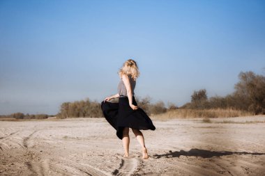 Genç bir Avrupalı kadın sahilde uzun siyah bir etek sallayarak dans ediyor. Özgürlük ve bağımsızlık hissi. Sınırsız olasılık. Hedefe doğru hareket et. Yaz mutluluğu.