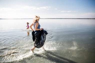 Anne ve kızı eğleniyor ve suda koşuyorlar. Mutluluk, özgürlük ve bağımsızlık durumu. Ebeveyn-çocuk ilişkilerini güçlendirmenin yanı sıra aile içinde fiziksel ve psikolojik sağlığın güçlendirilmesi..