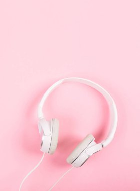 Pembe arka planda beyaz kulaklıklar. Müziğin üst görüntüsü. Etrafı sessiz, içi gürültülü. Yabancı sınırlara saygı. Dikey.
