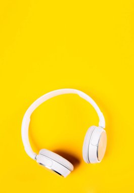Sarı arka planda beyaz kulaklıklar. Müziğin üst görüntüsü. Etrafı sessiz, içi gürültülü. Yabancı sınırlara saygı. Dikey.