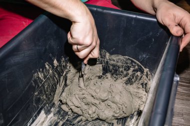 Bir insan, karışımı tamamlamak için çimento ve suyu bir kabın içine karıştırır. İnşaat süreci, dekorasyonun aşamalarından biri. Alçıtaşı yapıyorum. Yakın plan..