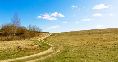 Kırsal bir toprak yol, güzel güneşli bir havada, ormanın kenarında, mavi gökyüzüne karşı kıvrılarak uzanır. İç dekorasyon için resim olarak kullanılabilir. Dokunulmamış doğa. Pankart