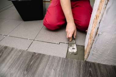 Kiremit döşemek için bir adam spatula ile çimento koyar. Bitirmek bir apartman dairesini onarmanın aşamalarından biridir. İşlem sırasında ellerin yakın plan görüntüsü.