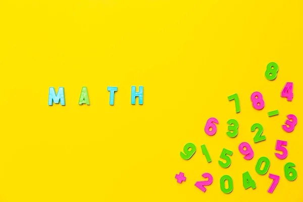 The word math is written on a yellow background in colored plastic toy letters. Nearby are numbers from zero to nine in a chaotic order. Wallpaper for notebooks or school market advertising banner.