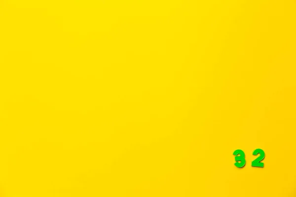 一个32号绿色塑料玩具放在一个黄色背景的右下角 — 图库照片