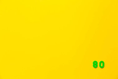 A green plastic toy number eighty is located in the lower right corner on a yellow background. clipart