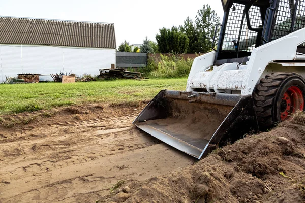 滑行转向装载机清理工地进行施工 国土整治方面的工作 在密闭地区工作的机器 带有运土桶 草皮和散装材料的小型拖拉机 — 图库照片