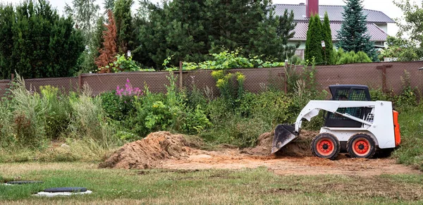 Bir patinaj dümeni yükleyicisi inşaat için alanı boşaltıyor. Arazi işleri arazi iyileştirmesi ile yapılır. Kapalı alanlarda çalışmak için bir makine. Toprak, çim ve malzeme taşımak için kovası olan küçük bir traktör..