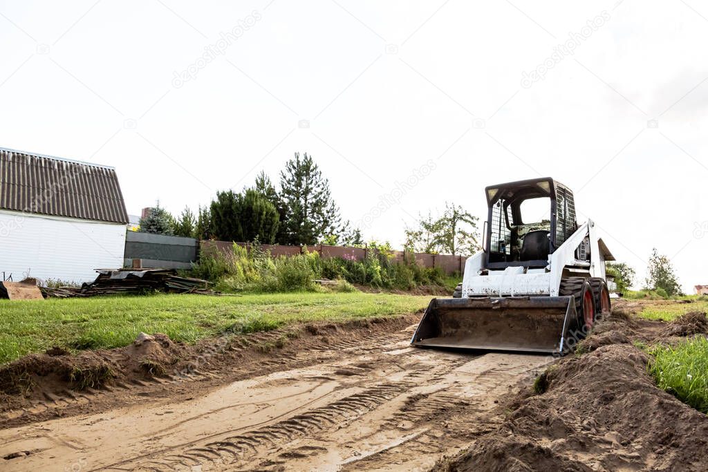 A skid steer loader clears the site for construction. Land work by the territory improvement. Machine for work in confined areas. Small tractor with a bucket for moving soil, turf and bulk materials.