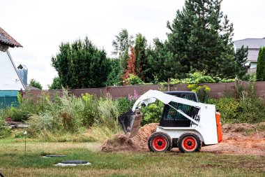 Bir patinaj dümeni yükleyicisi inşaat için alanı boşaltıyor. Arazi işleri arazi iyileştirmesi ile yapılır. Kapalı alanlarda çalışmak için bir makine. Toprak, çim ve malzeme taşımak için kovası olan küçük bir traktör..