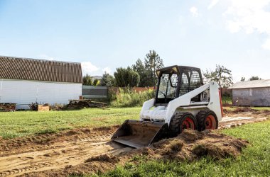 Bir patinaj dümeni yükleyicisi inşaat için alanı boşaltıyor. Arazi işleri arazi iyileştirmesi ile yapılır. Kapalı alanlarda çalışmak için bir makine. Toprak, çim ve malzeme taşımak için kovası olan küçük bir traktör..