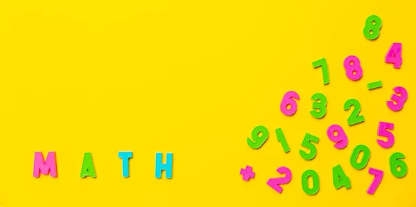 The word math is written on a yellow background in colored plastic toy letters. Nearby are numbers from zero to nine in a chaotic order. Wallpaper for notebooks or school market advertising banner.