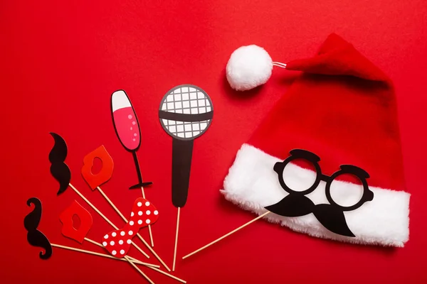 A red color banner with a Santa hat with a white pompom and a face from glasses and mustache. A props for entertaining guests at a New Year corporate festive or a karaoke party for a team of barbers.