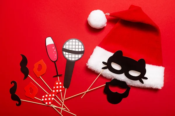 A red color banner with a Santa hat with a white pompom and a face from cat mask and mustache. A props for entertaining guests at a New Year corporate festive or a karaoke party for a team of barbers.