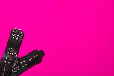 Pembe pankart, siyah deri pantolon askısı ve elleri ve bacakları kelepçelemek ve seks oyunları oynamak için metal perçin. BDSM deneği. Yetişkin ürünleri ve seks oyuncakları mağazası reklamı için arka plan.