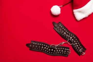 Siyah deri askılı kırmızı pankart ve kelepçeli eller ve bacaklar için metal perçinler ve seks oyunları. BDSM deneği. Yetişkin ürünleri ve seks oyuncakları mağazası reklamı için arka plan.
