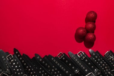Red banner with penis from christmas balls and black leather bracers and metal rivets for shackling hands or legs and sexual games. BDSM entertainment. Background for adult toy products or sex shop.