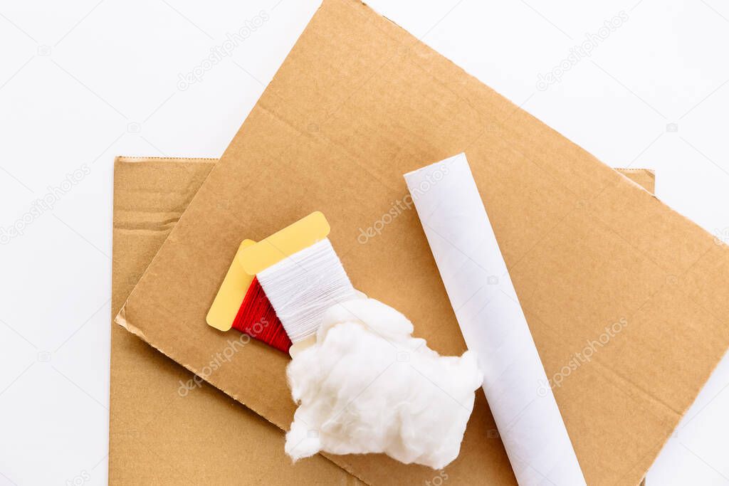 A sheets of brown cardboard, tube of paper towel, threads and wadding on a white background. Material for use in a step by step instruction for the manufacture of New Year's crafts, Christmas tree.