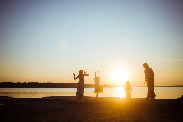 子供たちとその母親のシルエットがジャンプし 日没の光の中でビーチで楽しんでいます 若い世代と年配の世代の間で良い気分と娯楽 美しい風景 — ストック写真