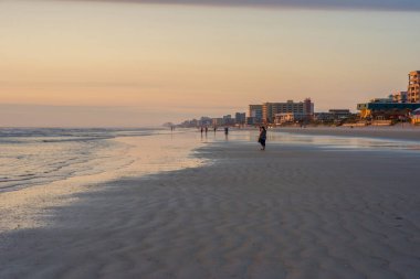 Sabahın erken saatlerinde okyanusta. İnsanlar kıyı boyunca yürür.