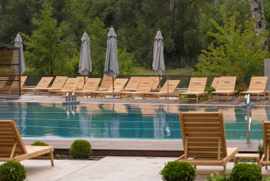 Şezlong. Havuzda mavi su. Güneş şemsiyeleri kapalı.