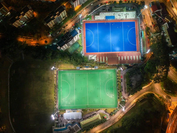 Aerial bird's eye view of the outdoor hockey field at night. The image contains soft-focus, grain, and noise.