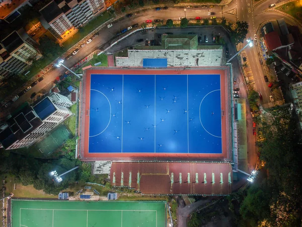 Aerial bird\'s eye view of the outdoor hockey field at night. The image contains soft-focus, grain, and noise.