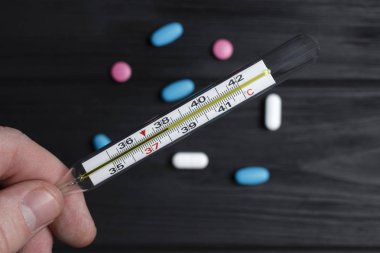 tatlı bir adam bir termometre ile yüksek bir sıcaklık elinde bir arka plan siyah bir ahşap arka plan üzerinde yalan çok renkli tablet tutuyor