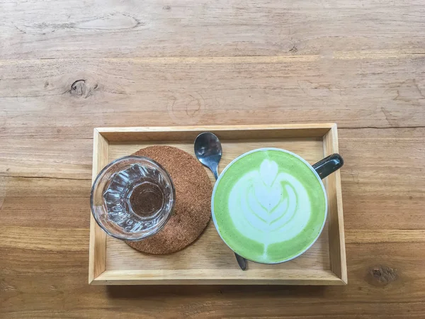 Ahşap masa üzerinde kopya alanı ile sıcak yeşil çay. Barista bardakta köpük ile latte sanat kalp şekli çizin. Üstten görünüm.