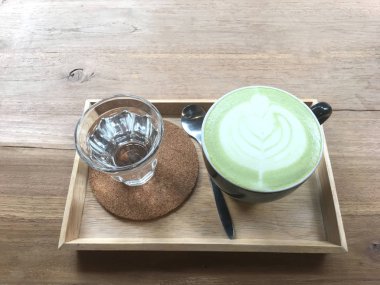 Ahşap masa üzerinde kopya alanı ile sıcak yeşil çay. Barista bardakta köpük ile latte sanat kalp şekli çizin. Üstten görünüm.
