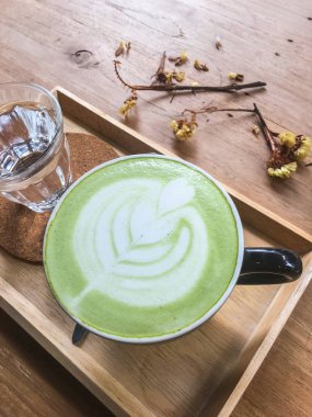 Ahşap masa ve kuru çiçek sıcak yeşil çay. Barista bardakta köpük ile latte sanat kalp şekli çizin. Üstten görünüm.