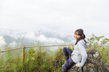 Asya kız rahatla ve yenileme dağ zemin üzerine yüksek dağlar, beyaz bulutlar ve sis bir manzara olduğunu.