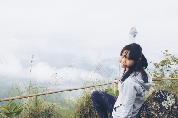 Asya kız rahatla ve yenileme dağ zemin üzerine yüksek dağlar, beyaz bulutlar ve sis bir manzara olduğunu.