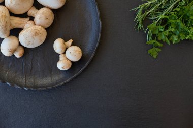 Yeşillikleri ile siyah bir tabakta champignon mantar