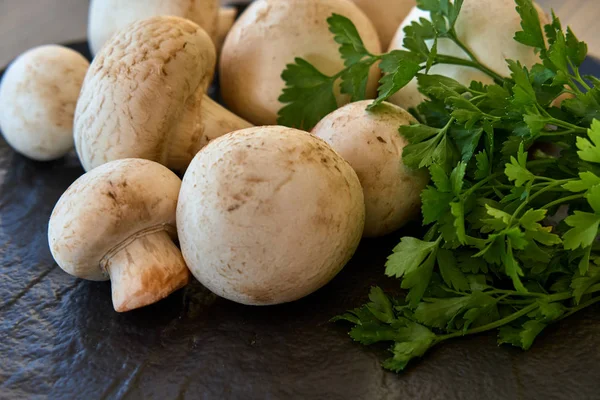 Yeşillikleri ile siyah bir tabakta champignon mantar